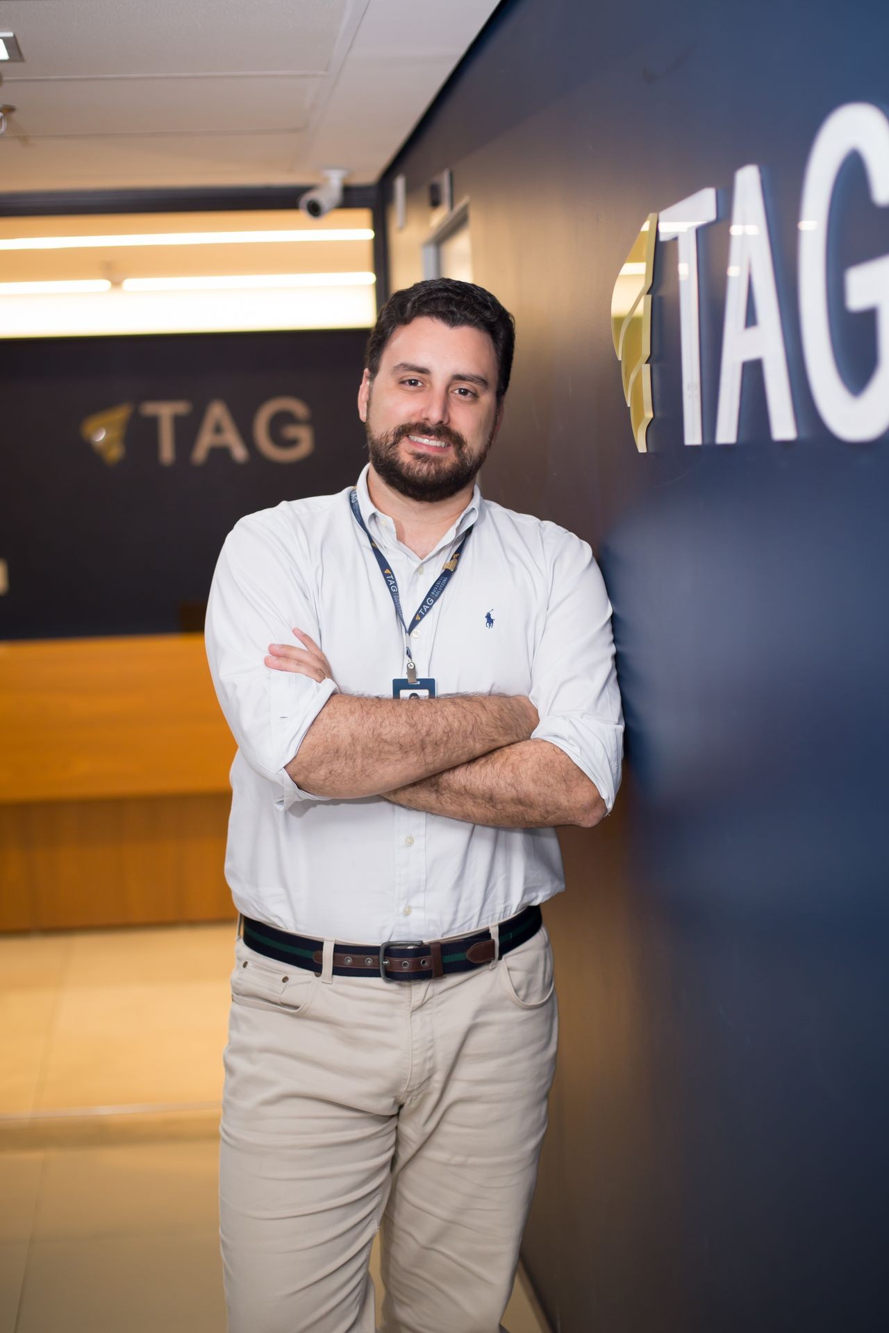 Man in white shirt leaning against a wall with the TAG logo in an office setting.